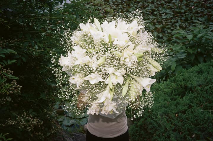 Person holding a bouquet of white flowers over their face