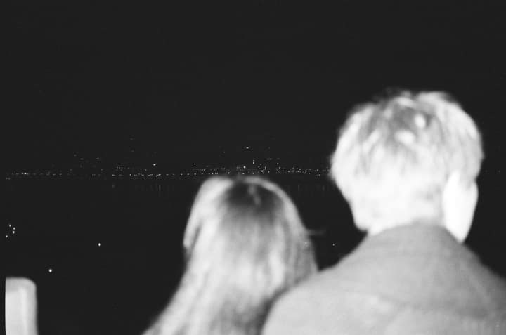 Backs of two people looking toward a dark river at night