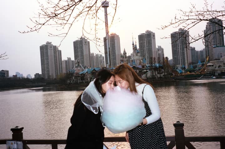 Two people standing near water with pink cotton candy