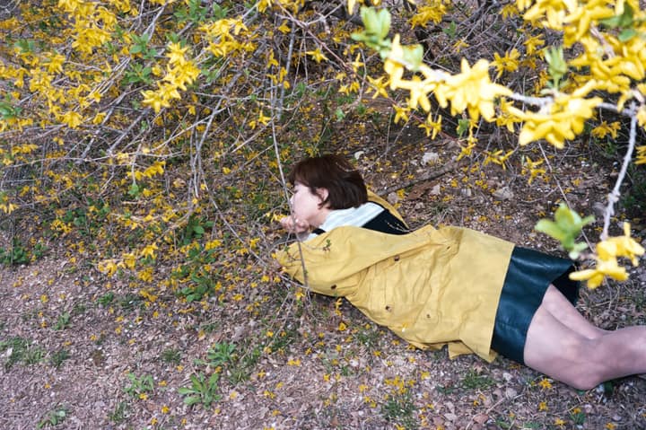 Person in a yellow coat lying near flowering branches