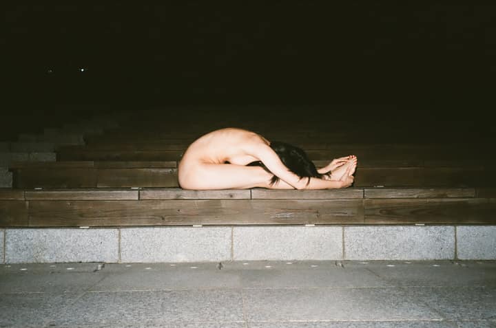 Nude figure curled on outdoor steps at night