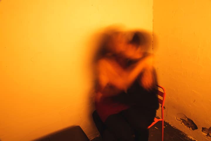Two people embracing in blurred motion against a warm yellow wall